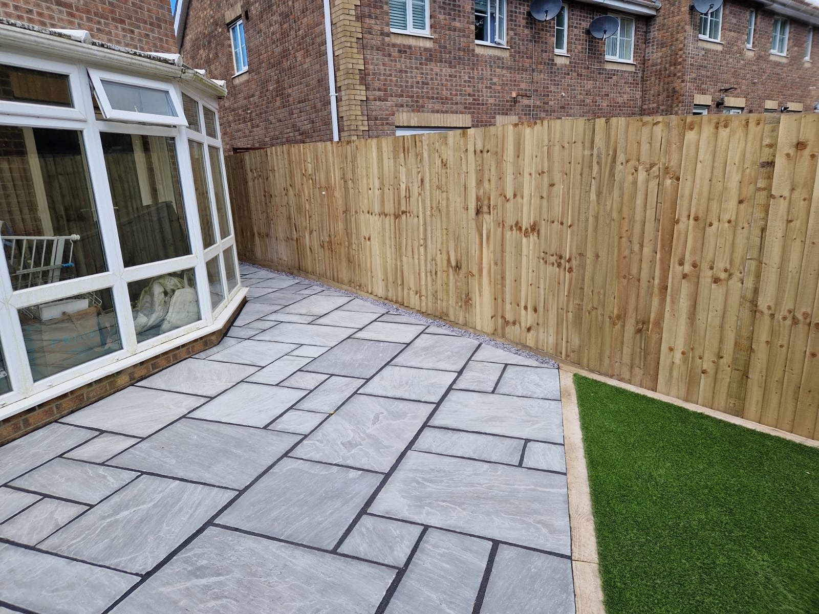 Grey sandstone patio beside a conservatory with new fencing